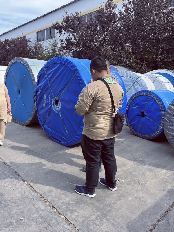Indonesia customer inspecting packed conveyor belt rolls during factory visit