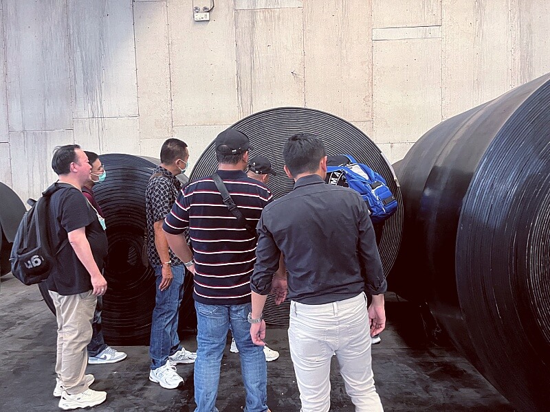Thailand customer inspecting finished conveyor belt rolls during factory visit