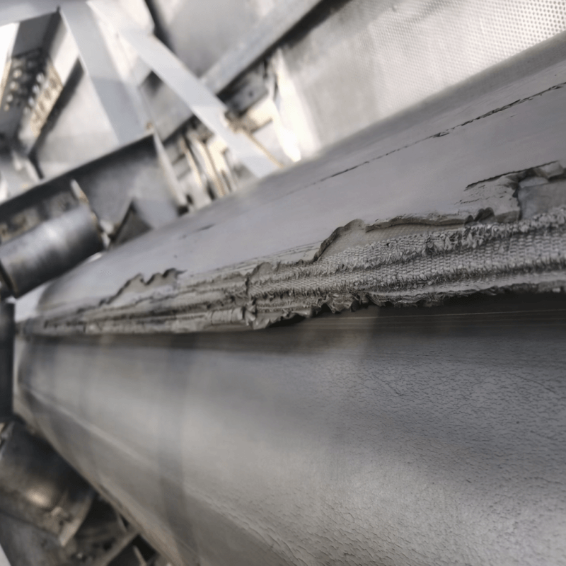 Worn pipe conveyor belt edge with exposed fabric layers due to improper transition distance and high edge tension