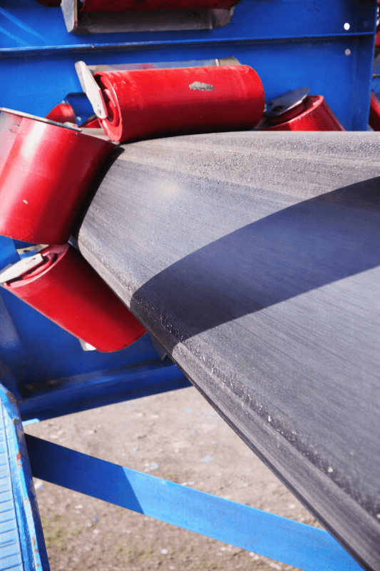 Pipe conveyor belt running over red idler rollers in enclosed bulk material conveying system