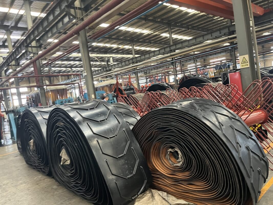 Large rolls of chevron conveyor belts in factory workshop for inclined bulk material conveying systems